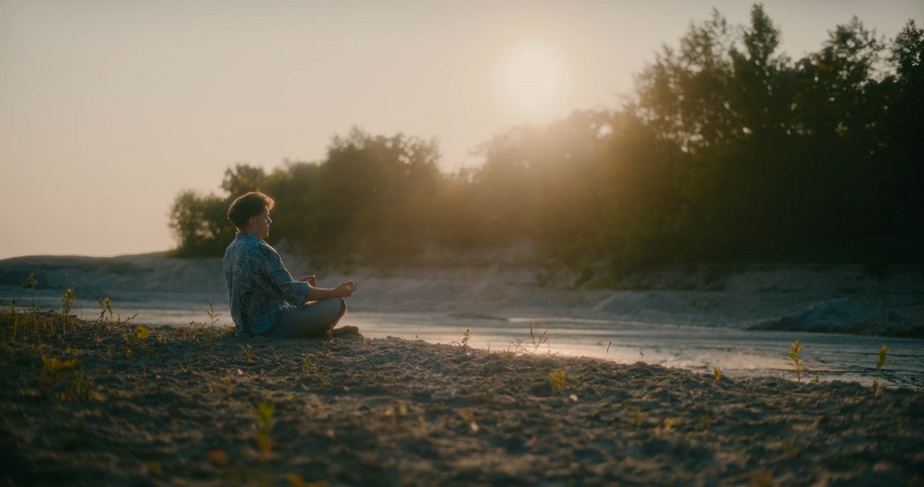 Muškarac sedi u meditativnoj pozi pored reke u prirodi
