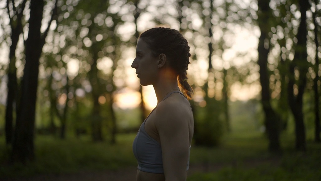 Žena u sportskoj opremi meditira okružena drvećem, joga u prirodi pri zalasku sunca