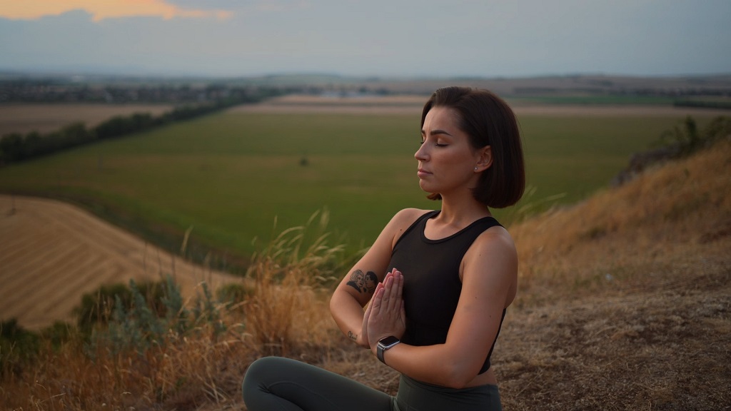 Sedeća meditacija sa sklopljenim dlanovima na proplanku s pogledom na dolinu